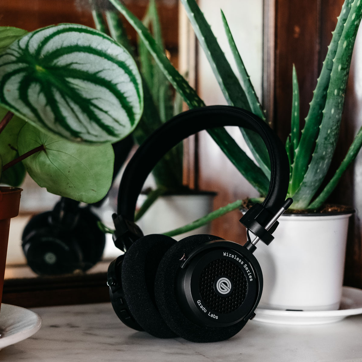 Photo of gw100 headphones resting on a marble table in front of plants