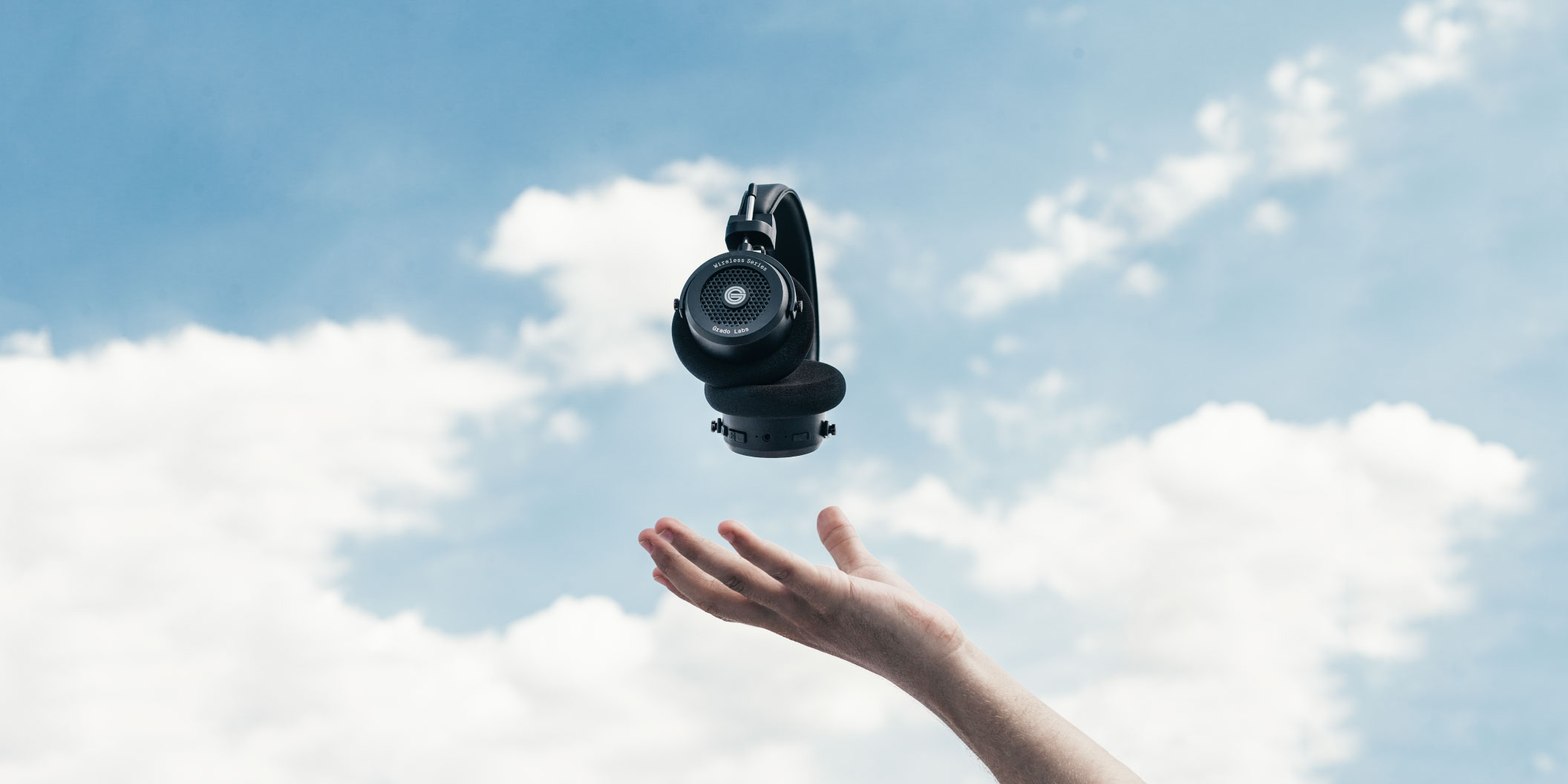 Photo of gw100 headphones levitating above a persons hand with a blue sky and clouds in the background