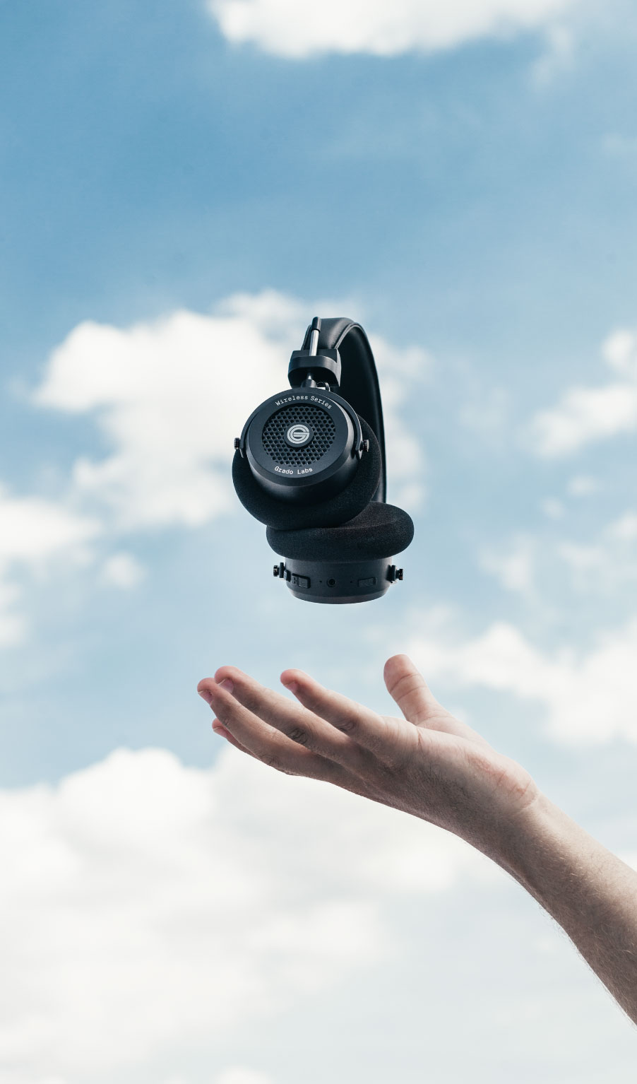 Photo of gw100 headphones levitating above a persons hand with a blue sky and clouds in the background
