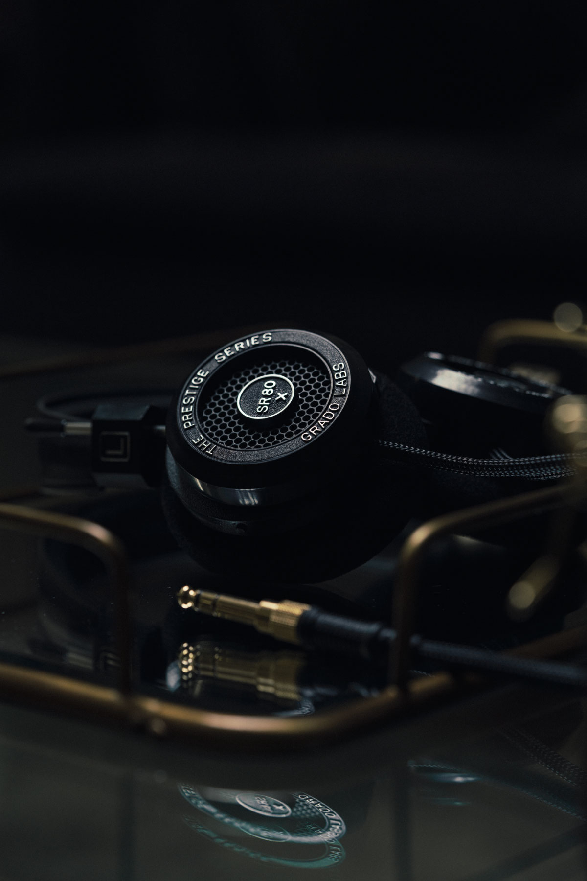 Photo of SR80x headphones resting on a reflective black table with an audio cable resting in front of the headphones